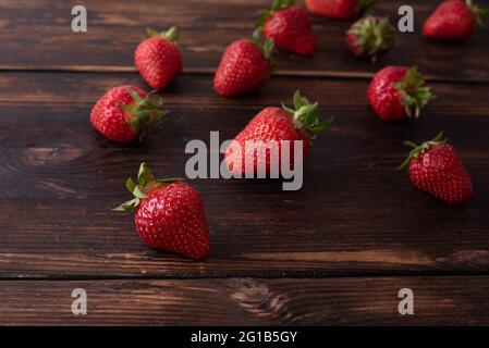 Reife Erdbeeren auf einem dunklen Holztisch gestreut, Sommerkonzept, Nahaufnahme. Stockfoto