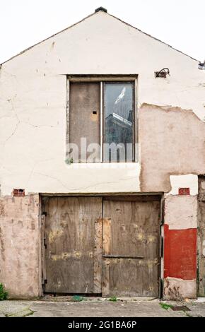 Vernachlässigtes Gebäude mit blockiertem Fenster und breiter Holztür darunter Stockfoto