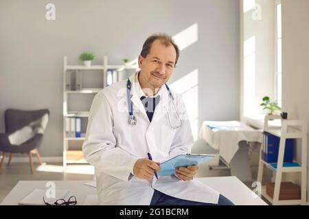 Porträt eines erfahrenen männlichen Oberarztes mit Dokumenten in den Händen im Klinikbüro. Stockfoto