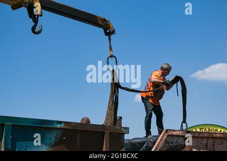 Dnepropetrovsk, Ukraine - 05.28.2021: Müllcontainer mit einem Kran in einen LKW laden. Slinger funktioniert. Stockfoto