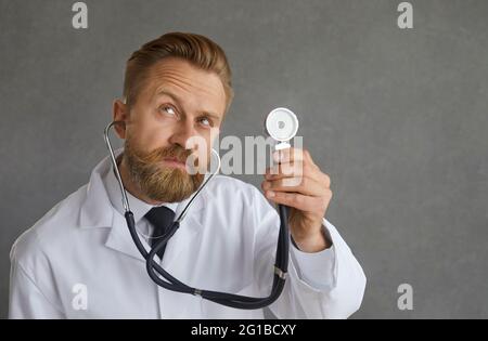Porträt eines männlichen Arztes, der Stethoskop hält und dem Herzschlag des Patienten zuhört Stockfoto