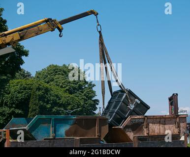 Verladen von Müllcontainern mit einem Kran in einen LKW. Slinger funktioniert. Stockfoto