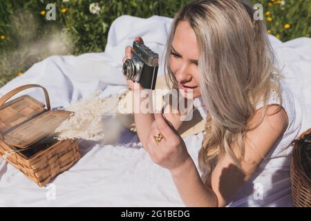 Von oben eine positive Frau, die am Sommertag auf dem karierten Boden liegt und Fotos mit einer altmodischen Kamera auf dem Land fotografiert Stockfoto