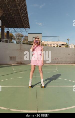 In voller Länge fröhlich fit weiblich in rosa sundress Skaten auf Rollen fotografieren auf Instant-Foto-Kamera auf sonnigen Sportplatz Stockfoto