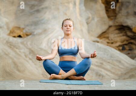 Junge, achtsame Frau in Sportkleidung, die mit geschlossenen Augen meditiert, während sie Yoga auf steinigem Hintergrund praktiziert Stockfoto