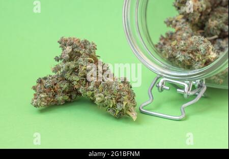 Trockene Knospen von Marihuana in einem Glasgefäß in Nahaufnahme auf grünem Hintergrund. Stockfoto