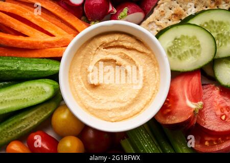 Schale mit hausgemachtem Hummus, serviert auf dem Teller mit verschiedenen frischen, farbenfrohen Gemüsesorten Stockfoto