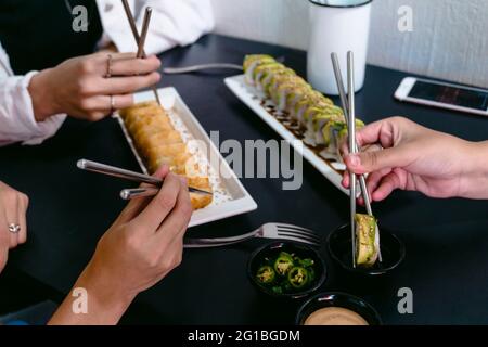 Anonyme Freunde aus einem hohen Blickwinkel mit wiederverwendbaren Essstäbchen, die köstliche Sushi-Brötchen mit Sojasauce und Jalapeno-Pfeffer essen Stockfoto