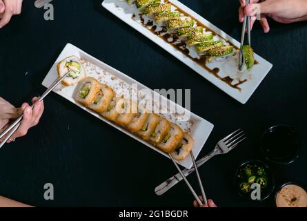 Anonyme Freunde aus einem hohen Blickwinkel mit wiederverwendbaren Essstäbchen, die köstliche Sushi-Brötchen mit Sojasauce und Jalapeno-Pfeffer essen Stockfoto