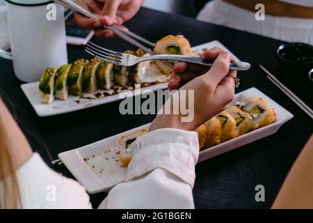 Anonyme Freunde aus einem hohen Blickwinkel mit wiederverwendbaren Essstäbchen und Gabel, die leckere Sushi-Brötchen mit Sojasauce und Jalapeno-Pfeffer essen Stockfoto