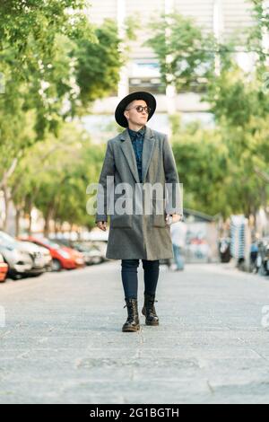 Junge Transgender-Person in edlem Mantel und Hut, die bei Tageslicht wegschaut Stockfoto