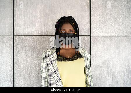 Enttäuschte afroamerikanische Frau in Maske, die gegen eine graue Wand stand und mit Traurigkeit auf die Kamera schaute Stockfoto