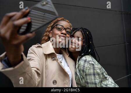 Junge lächelnde afroamerikanische Freundinnen, die nahe stehen und sich auf dem Handy selbst porträtieren Stockfoto