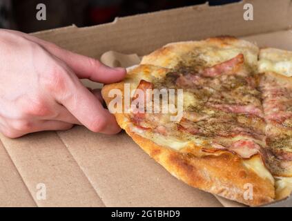 Eine Frau nimmt eine Scheibe Pizza mit Speck. Nahaufnahme. Stockfoto