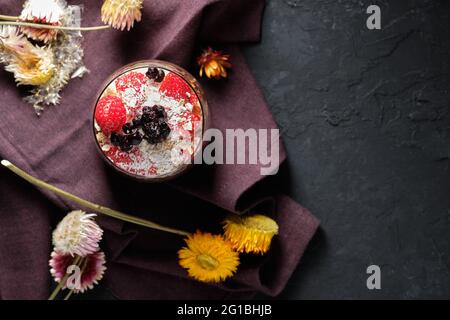 Draufsicht appetitliche Smoothie-Schale mit Granola-Erdbeeren und Heidelbeeren auf dem Tisch in der Nähe verschiedener Wildblumen Stockfoto