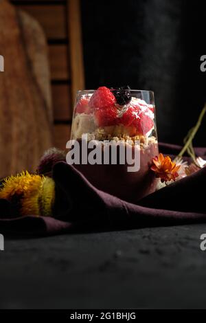 Appetitliche Smoothie-Schale mit Granola-Erdbeeren und Heidelbeeren auf dem Tisch in der Nähe verschiedener Wildblumen Stockfoto
