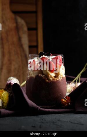 Appetitliche Smoothie-Schale mit Granola-Erdbeeren und Heidelbeeren auf dem Tisch in der Nähe verschiedener Wildblumen Stockfoto