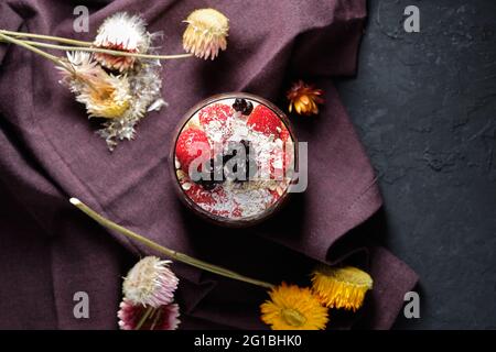 Draufsicht appetitliche Smoothie-Schale mit Granola-Erdbeeren und Heidelbeeren auf dem Tisch in der Nähe verschiedener Wildblumen Stockfoto