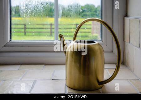 Auf einer gefliesten Küchenfensterschwelle sitzt ein dekorativer goldfarbener Krug mit einem großen, durchgeschleiften Griff. Stockfoto