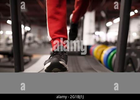 Crop anonymen männlichen Athleten in Sportbekleidung und Sneakers laufen auf dem Laufband während des Fitnesstrainings in modernen Fitness-Studio Stockfoto