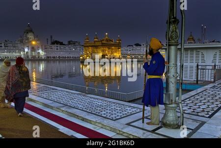 Amritsar, Indien - 06. November 2016: Ein nicht identifizierter Besucher und Pilger, die am Teich spazieren, und ein männlicher sikh-Wachmann am berühmten Goldenen Tempel, Stockfoto