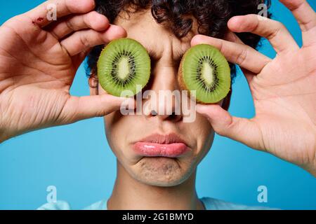 Mann mit lockigem Haar, der Kiwi in der Nähe des Klassengesichts hält Emotionen Stockfoto