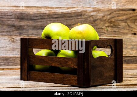 Eine Holzkiste mit reifen grünen Äpfeln auf dem Holztisch Stockfoto