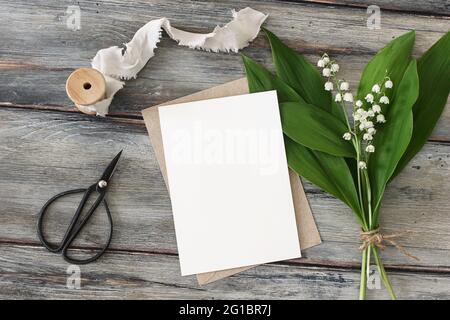 Hochzeitsbriefpapier im Frühling. Leere Grußkarte, Einladungsmockup. Schwarze Vintage Schere, Seidenband und Bouquet von blühenden lilly of the Valley Stockfoto