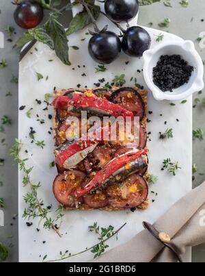 Sardine in Olivenöl, Toast mit schwarzen Tomaten und Kräutern auf Marmorplatte Stockfoto