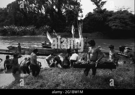 West Kalimantan, Indonesien. März 2007. Ein Mann wirft ein Gamelan-Schlaginstrument aus, während er an einer Menschenmenge vorbeiläuft – der Dayak Tamambaloh Community – die sich als reinigenden Akt mit Wasser überspritzt. vor einem Boot, das gerade die Familie ihres neuen traditionellen Häuptlings für einen Besuch der Grabstätte ihres ehemaligen Häuptlings in Sungai Uluk Palin (Sungulo Palin) Dorf, Putusibau Utara, Kapuas Hulu, West Kalimantan, Indonesien, transportiert hat. Stockfoto