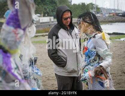 Vancouver, Kanada. Juni 2021. Ein Mann sieht sich am 6. Juni 2021 eine Figur an, die aus Kunststoff am Kitsilano Beach in Vancouver, British Columbia, Kanada, hergestellt wurde. Die von der multidisziplinären Künstlerin Caitlin Doherty geschaffenen Figuren, die aus Plastik an kanadischen Küsten entfernt wurden, verkörpern den kollektiven Beitrag der Menschen zur Plastikverschmutzung und bringen das Thema der Küstenverschmutzung in den Vordergrund. Quelle: Liang Sen/Xinhua/Alamy Live News Stockfoto