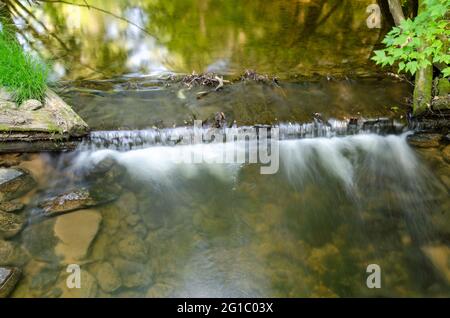 Lange Exposition von Wasser, das über ein Wehr in einem Bach kaskadiert Stockfoto