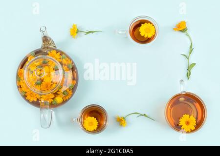 Rahmen aus Tassen Kräutertee, transparenter Teekannen und Ringelblumen auf blauem Hintergrund. Beruhigendes Getränkekonzept. Kopierbereich Draufsicht Flat Lay. Stockfoto