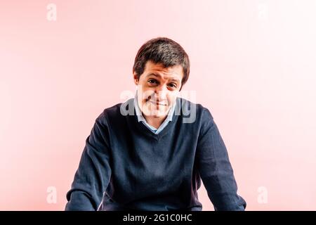 Junger erwachsener Mann im Alter von 35 Jahren mit Hemd und blauem V-Ausschnitt-Pullover mit rosa Hintergrund, der geradeaus lächelt. Stockfoto
