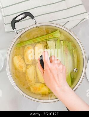 Frau Hand legt Deckel auf Pfanne, Nahaufnahme von oben, vertikales Banner. Sellerie Suppe Schritt für Schritt Rezept Stockfoto