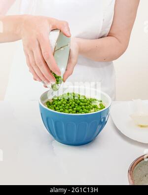 Grüne Erbsen in einer Schüssel. Schritt für Schritt cremig pürierte Sellerie-Suppe mit frischen grünen Erbsen Rezept, Frau Hände, vertikale Banner Stockfoto