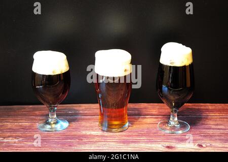 Drei Gläser mit verschiedenen dunklen Biersorten stehen auf einem Holztisch. Nahaufnahme. Stockfoto