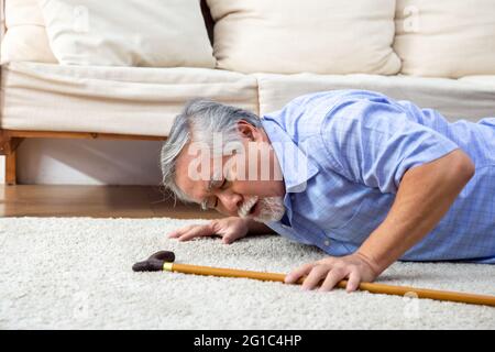 Asiatischer älterer Mann, der auf Teppich fiel und im Wohnzimmer zu Hause auf dem Boden lag, Konzept „Falls of older adults“ Stockfoto