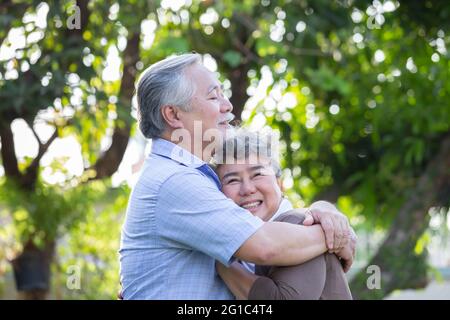 Glückliches reifes Paar verliebt umarmen und lachen im Garten, asiatische Senior umarmt im Freien und feiert Hochzeitstag Stockfoto