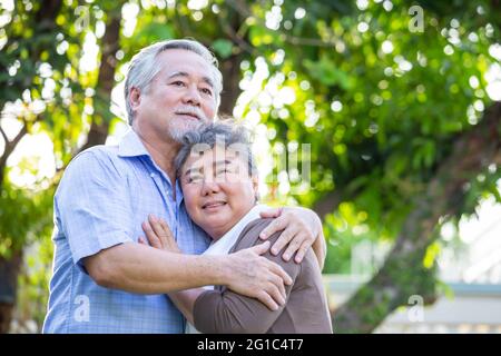 Glückliches reifes Paar in der Liebe umarmt im Garten, asiatische Senior umarmt im Freien und feiert Hochzeitstag Stockfoto