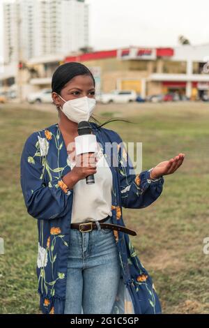 Afrikanische Reporterin in Maske spricht in Mikrophon auf der Straße in der Stadt Stockfoto