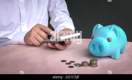 Geschäftsmann mit Taschenrechner mit gestapelten Münzen und Sparschwein auf dem Schreibtisch. Speicherplatz kopieren. Stockfoto