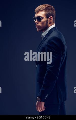 Seitenansicht eines Fashion bärtigen jungen ernsthaften Mannes in Sonnenbrille, Luxusanzug mit einer Hand in der Tasche Stockfoto