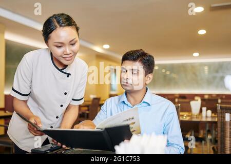 Reifer Mann, der mit der Kellnerin spricht und sie bittet, ihm das Tagesgericht von der Speisekarte zu bringen Stockfoto