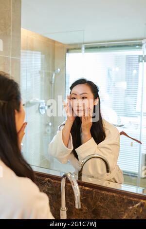 Schöne junge Frau, die Hautpflege vor dem Badezimmerspiegel nach der morgendlichen Dusche Stockfoto