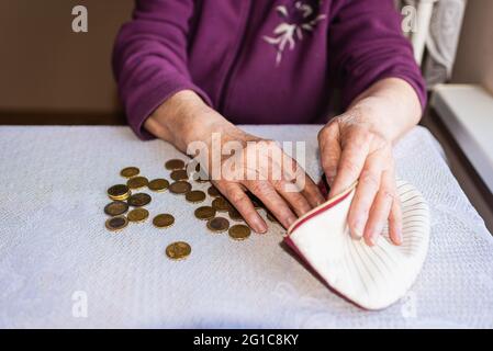 Besorgte ältere Frau, die zu Hause sitzt und die verbleibenden Münzen zählt.alt Frau, die zu Hause kläglich am Tisch sitzt und zählt Verbleibende Münzen für Stockfoto