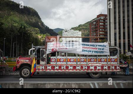 Bogota, Kolumbien. Juni 2021. Eine 'Chiva' der indigenen Gemeinschaften von Misak mit kolumbianischer Flagge und einem Schild mit der Aufschrift 'das Blut unserer Kämpfer bittet um Gerechtigkeit' und 'Wir sind die Wurzeln und Ausbrüche im Widerstand in Zeit und Raum', während sich Menschen und indigene Gemeinschaften von Misak versammeln, um auf die Ankunft von zu warten Die Interamerikanische Kommission für Menschenrechte (CIDH) inmitten von Polizeibrutalität und Unruhen während regierungsfeindlicher Proteste, die am 6. Juni 2021 in Bogota, Kolumbien, mindestens 70 Tote erreichten. Kredit: Long Visual Press/Alamy Live Nachrichten Stockfoto