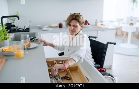 Portrait der behinderten reifen Frau im Rollstuhl drinnen zu Hause, Vorbereitung Frühstück. Stockfoto