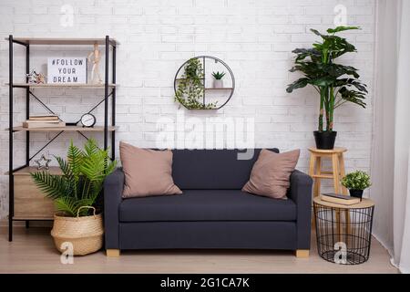 Stilvolle Einrichtung mit Sofa, Tisch und Regal über Backsteinwand Stockfoto