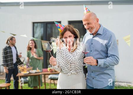 Reifes Paar mit Wein im Freien im Garten zu Hause, Geburtstagsfeier. Stockfoto